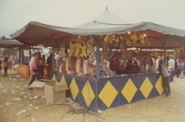 A carnival game at a midway under a tented canvas cover, there are colourful stuffed animal toys hung all around as prizes