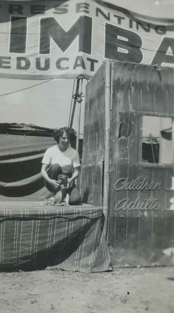 Black and white photo of a woman handling a monkey in front of a banner that says Presenting Simba, a ticket sales box is beside her