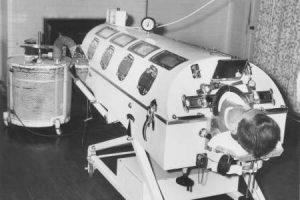Black and white photo of a person inside an Iron Lung, a large cylinder shaped coffin like machine
