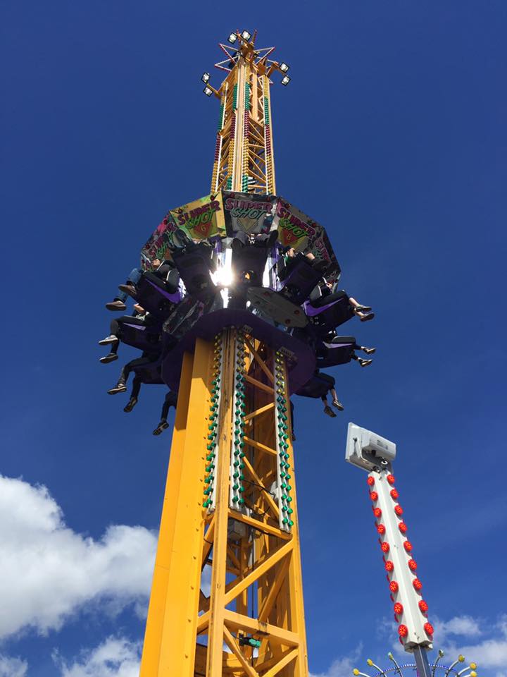 A carnival thrill ride that goes up and plunges downwards, people's leg are flailing above while seated as the ride goes up, Super Shot can be read all around the ride