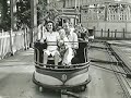 Black and white thumbnail sized picture of people riding a carnival ride inside a ride bucket on a track
