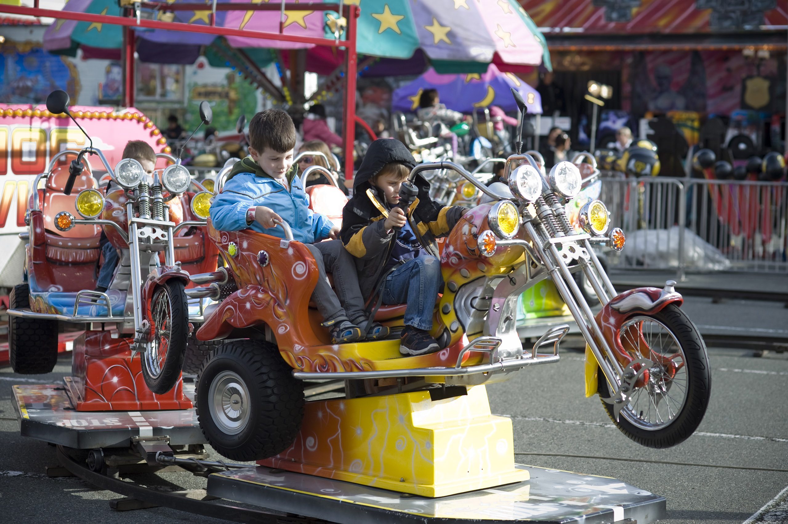 Two young boys riding a kiddie ride that is a motorcycle on a track at a carnival midway