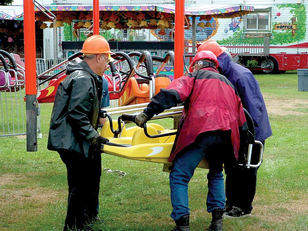 Four men wearing hard hats are lifting and moving a carnival ride bucket