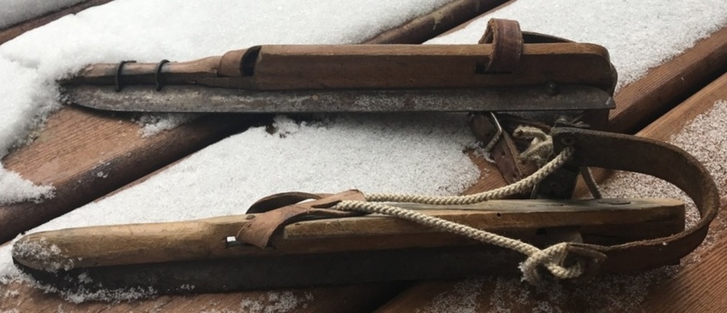 Close up of old vintage speed skates, no actual shoe attached, just rope and leather straps attached to wood with a blade at the bottom