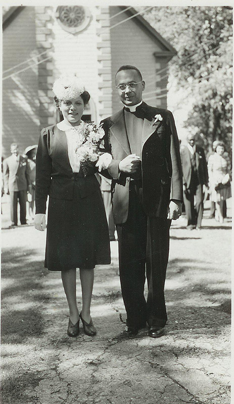 Black and white photograph of Esther Taylor (left) and her husband Rev Burgess (right) standing in front of St Peter's church on their wedding day.