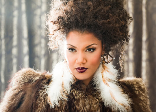 Colour portrait photograph of a Black woman with curly hair wearing a fur coat.