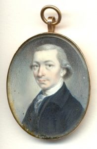Gold locket with a painting of a man with white hair wearing a black jacket with a white scarf.