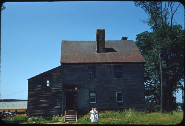 Colour photograph of two women standing in front an old house.