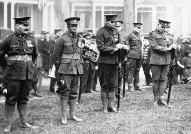 Black and white archival photo of WWI veterans standing in rows with one Black soldier looking at the camera.