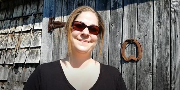 Recent colour photo of Jennifer Dow standing in front of a barn door with a horseshoe hanging from it.