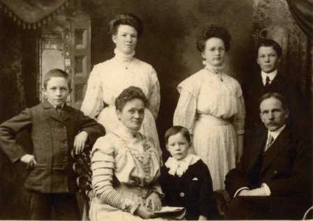 A family of seven grouped together wearing formal clothes.