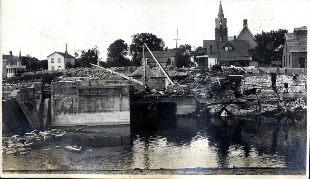 Construction on a river bank and in the river, a church can be seen in the background.
