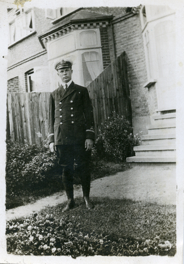 A man in a pilot’s uniform standing in front of a wooden fence.