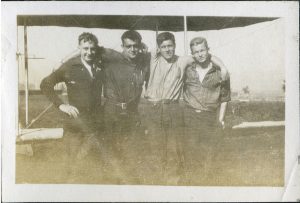 Quatre hommes posent en groupe compact devant un biplan.