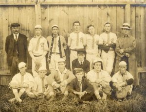 Quatorze hommes en uniforme de sport forment deux rangées devant une palissade en bois. 