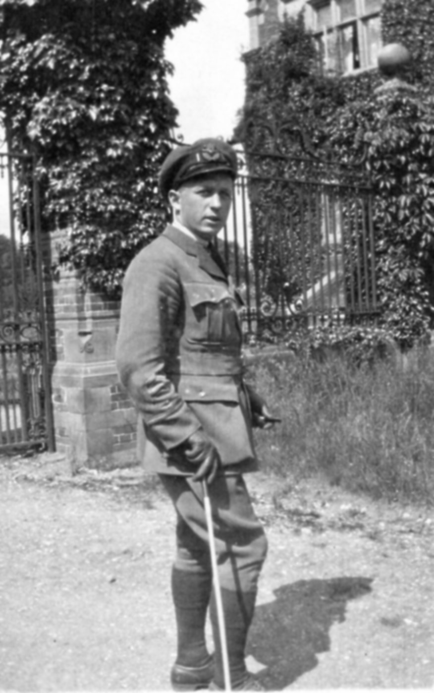 A man dressed in a military uniform standing casually in front of an iron fence outside of a house.