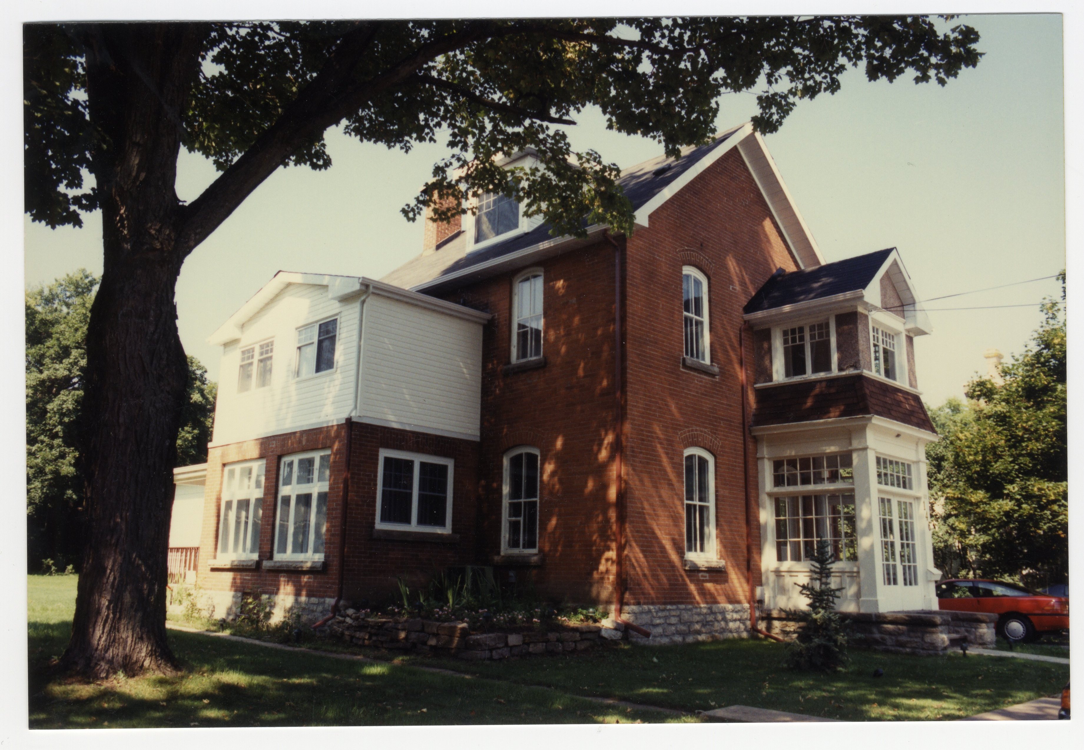 A large two and a half storey red brick house with a glassed in veranda.