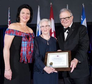 Three formally dressed people stand together holding a framed certificate.