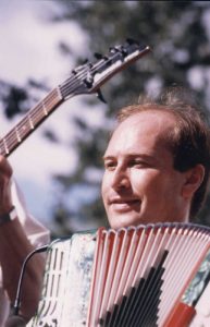 Close-up colour photograph of Bernard Félix and his accordion, with the neck of a bass guitar in the background.
