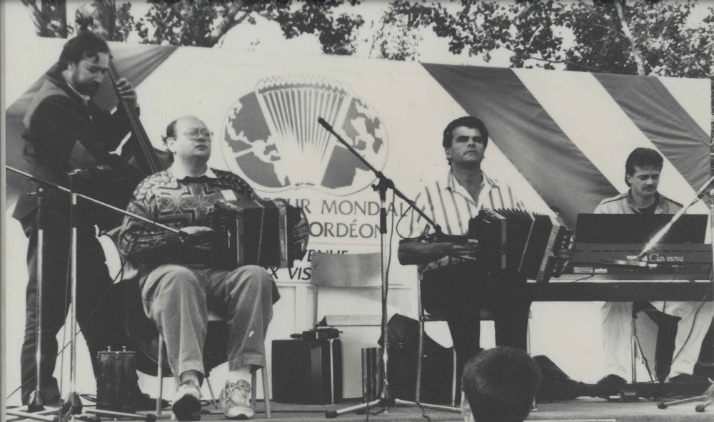 Photographie noir et blanc où quatre musiciens sur scène sont concentrés sur leur performance. À l’arrière-plan, on voit, le logo du Carrefour mondial de l'accordéon. 