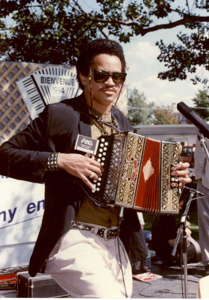 Colour photograph of Joaquin Diaz holding his diatonic accordion as he plays outdoors on a lovely sunny day.