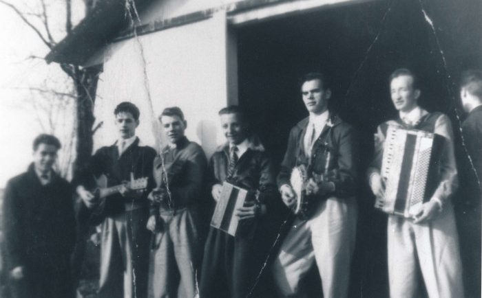 Black and white photograph of a seven-man band posing in front of a sugar shack.