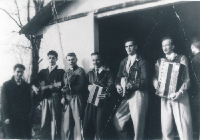 Black and white photograph of a seven-man band posing in front of a sugar shack.