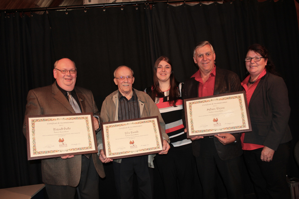 Colour photograph of five people, all of whom are standing. Three individuals are holding certificates of appreciation, which have been presented by the two others.