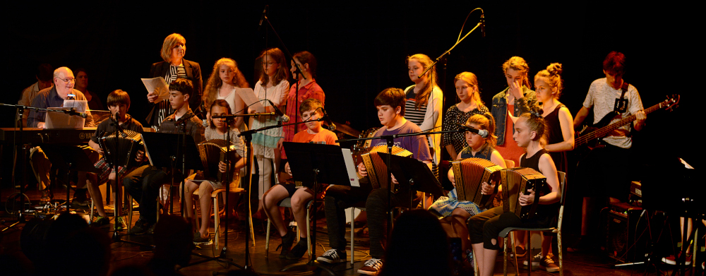 Color photography, several young school-aged musicians perform a concert on a stage.