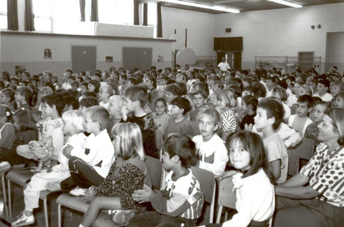 Black and white photograph of a large group of elementary school children gathered for an accordion concert.