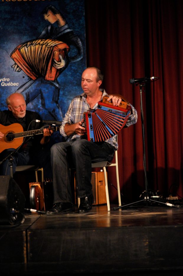 Colour photograph of Stéphane Landry playing diatonic accordion. Bruno Gendron is playing acoustic guitar in the background.