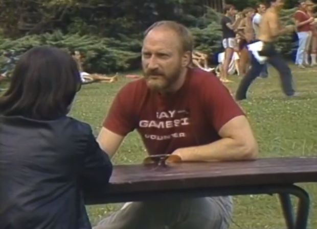 Tom Waddell is interviewed by Mary Anne McEwen about the origin of the Gay Games. They are sitting on a park picnic table at a venue of the 1983 Vancouver Gay Summer Games.