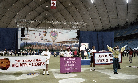 The Lesbian and Gay Bands of America perform on the floor of B.C. Place Stadium at the Closing Ceremonies. Banners for the Lesbian and Gay Big Apple Corps and the Flamingo Freedom Band dominate the foreground.