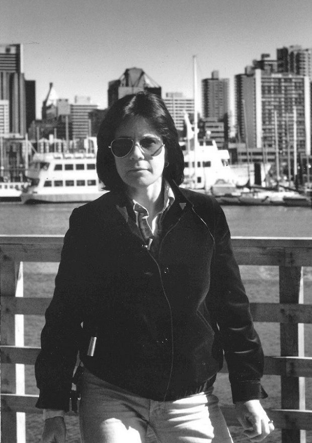 Black and white photo of Mary Anne McEwen on the Vancouver waterfront with the city behind her, c.1983.