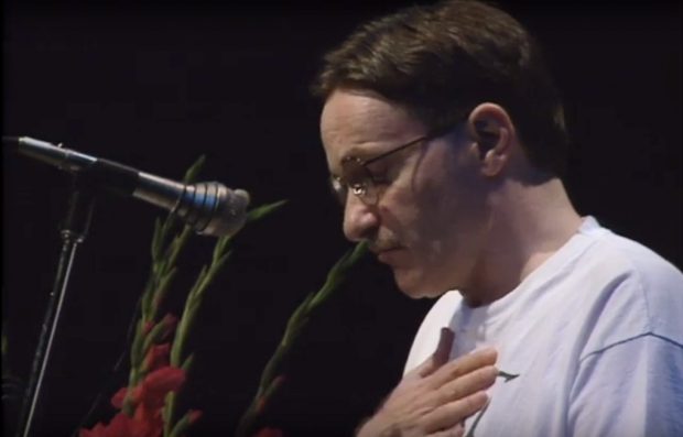 Writer Yves Navarre stands on a stage in front of a microphone with papers in his hands reading from his work.