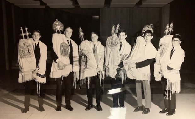 A black-and-white photograph of 6 teenage boys wearing prayer shawls and carrying Torah scrolls.