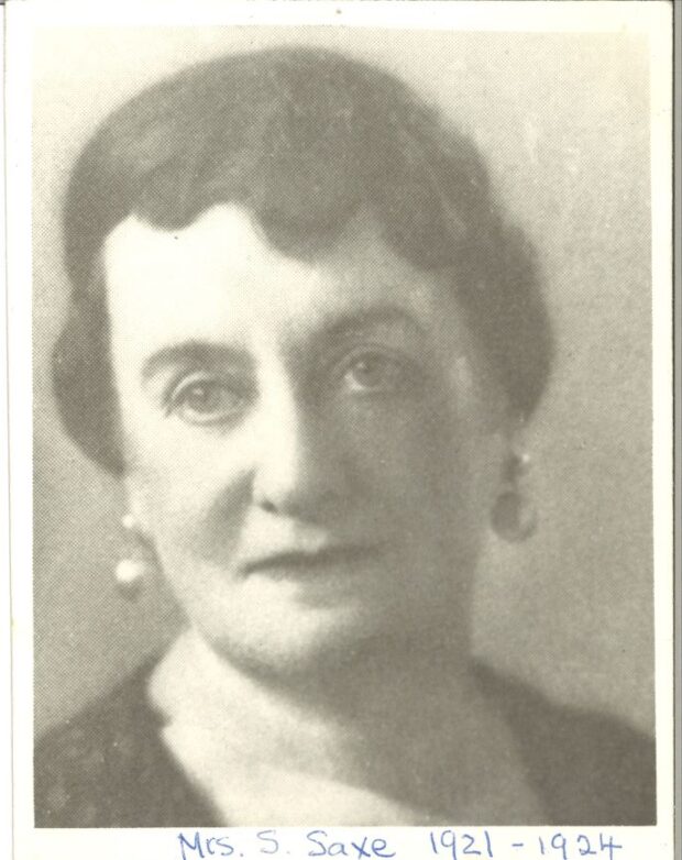 A black-and-white photograph of a middle-aged woman with pulled back hair and earrings.