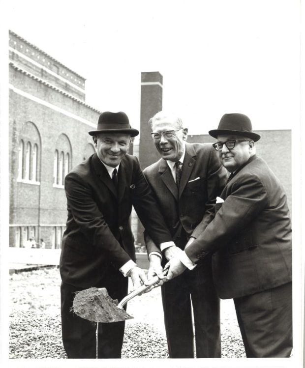 a black-and-white-photograph of three men in suits holding a shovel.