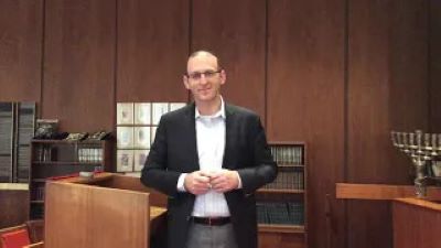 A rabbi wearing a suit, standing in a synagogue chapel.