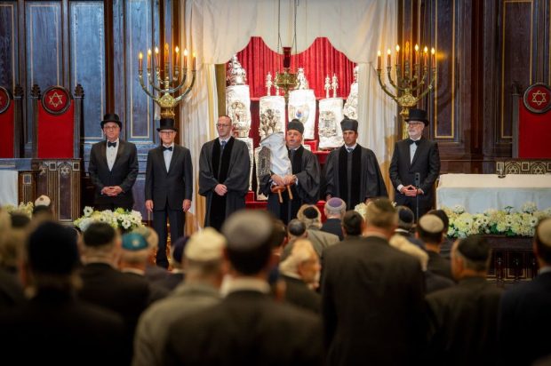 A group of men dressed in formal and ceremonial standing on a synagogue bimah for a rededication ceremony.