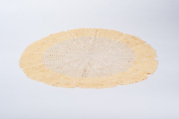 A round crocheted centrepiece on a white background. The outside is very pale yellow and the inside is light beige. The stitches form a twelve-point star pattern.