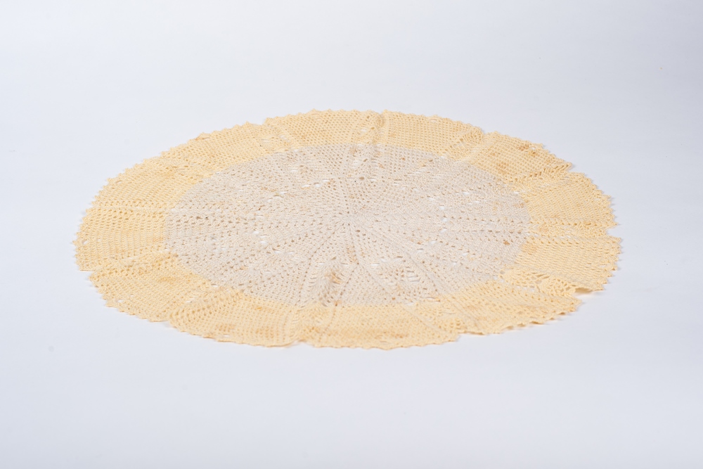 A round crocheted centrepiece on a white background. The outside is very pale yellow and the inside is light beige. The stitches form a twelve-point star pattern.