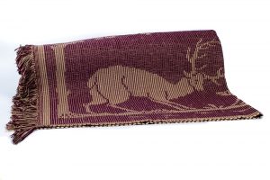 A fringed burgundy and beige catalogne folded in two. The visible half shows a deer.