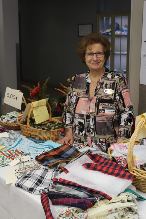 A smiling woman is standing behind a table on which coloured net and cloth bags for bulk foods are displayed.