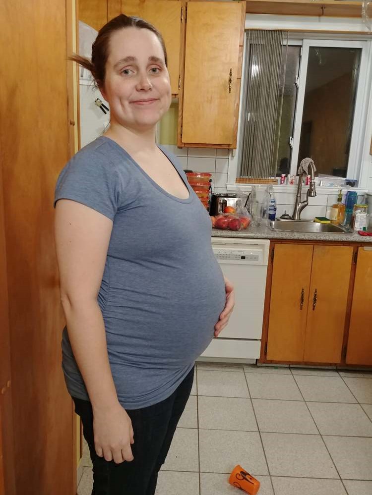 A woman who is several months pregnant poses in her kitchen.