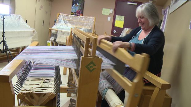 A women is working at a loom. She pulls a ros towards her.