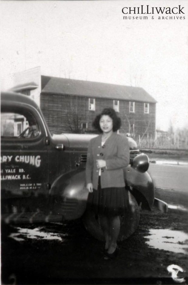 Dorothy Kostrzewa stands in front of her brother's company truck. Behind her is the Chinese Masonic Hall.