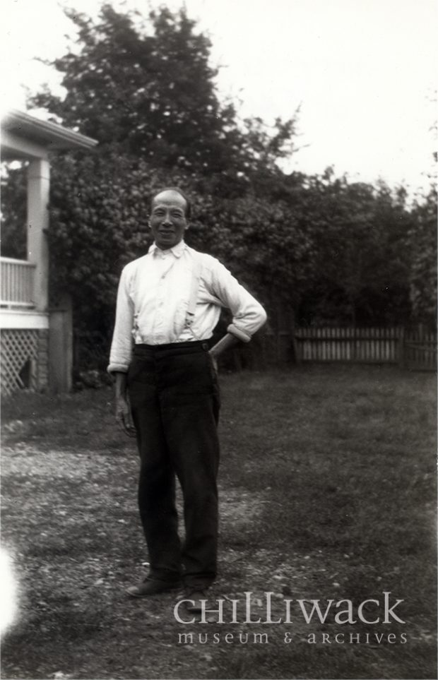 Chinese-Canadian worker standing in front of a shed with the left hand on his hip.