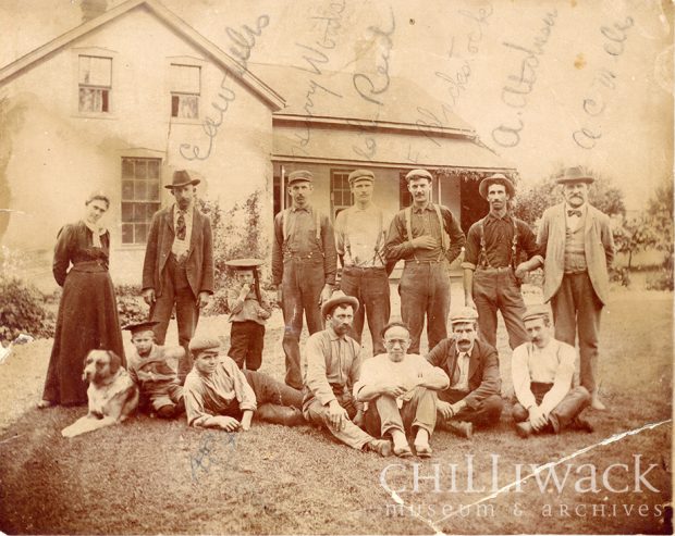 Group portrait of Edenbank farm workers and families in two rows in front of house.