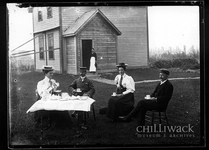Portrait of two women and two men seated having tea in front of Hulbert house with Chinese domestic worker in background